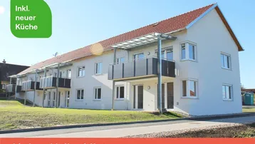 Modernes Mehrfamilienhaus mit mehreren Balkonen und gepflegter Grünfläche unter blauem Himmel.