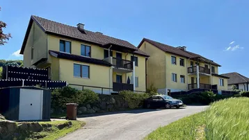 Mehrere Wohngebäude mit gelber Fassade, braunen Ziegeldächern und Balkonen in ländlicher Umgebung.