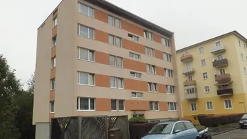Mehrstöckiges Wohngebäude mit gestreifter Fassade und parkenden Fahrzeugen davor in städtischer Umgebung.