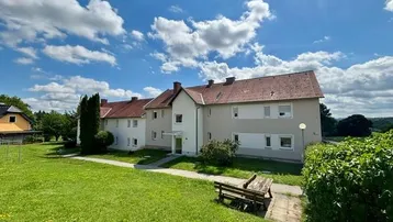 Mehrfamilienhaus mit Satteldach und gepflegter Grünfläche unter blauem Himmel.