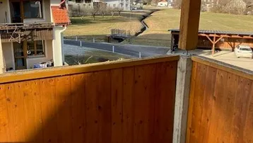 Balkon mit Holzgeländer und weitem Blick über die grüne Landschaft und die umliegenden Berge.
