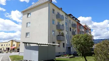 Mehrfamilienhaus mit Balkonen und Grünflächen unter blauem Himmel, das einen gepflegten Eindruck macht.