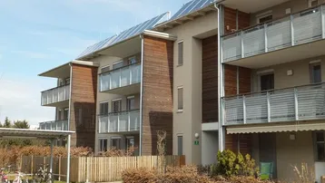 Modernes Mehrfamilienhaus mit Balkonen, Holzfassade und Photovoltaikanlage auf dem Dach.