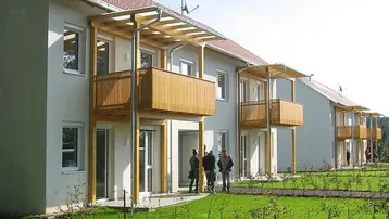 Moderne Reihenhäuser mit Balkonen und Terrassen, umgeben von einer gepflegten Grünfläche.