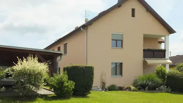 Einfamilienhaus mit Carport, Garten und Balkon in ländlicher Umgebung.