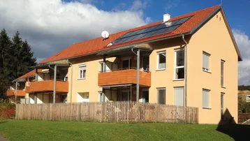 Modernes Mehrfamilienhaus mit beiger Fassade, Balkonen und Photovoltaikanlage auf dem Dach.