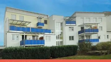 Modernes Mehrfamilienhaus mit mehreren Balkonen, großen Fenstern und gepflegter Grünanlage im Vordergrund.