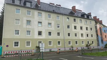 Mehrfamilienhaus mit heller Fassade und Satteldach in einer grünen Umgebung.