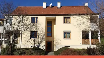 Mehrfamilienhaus mit heller Fassade und rotem Ziegeldach in sonniger Umgebung.