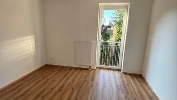 Leeres Zimmer mit Laminatboden und Zugang zu einem französischen Balkon.