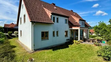 Großzügiges Einfamilienhaus mit Satteldach und weitläufigem Gartenbereich unter blauem Himmel.