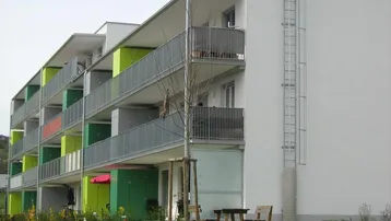 Modernes Mehrfamilienhaus mit farbigen Balkonen und gepflegter Grünfläche im Vordergrund.