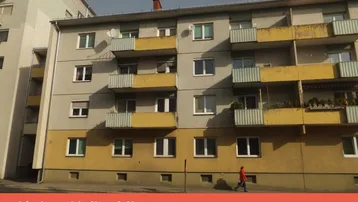 Fassade eines älteren Mehrfamilienhauses mit mehreren Balkonen und einer Werbebotschaft am unteren Rand.