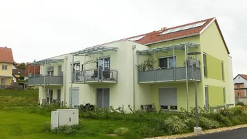 Modernes Mehrfamilienhaus mit Balkonen, Photovoltaikanlage und grüner Fassade in ländlicher Umgebung.