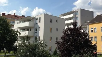 Modernes Mehrfamilienhaus mit hellgrauer Fassade und Balkonen unter blauem Himmel.