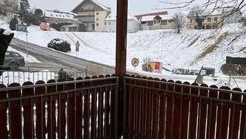 Balkon mit Holzboden und Blick auf die verschneite Umgebung und Häuser.