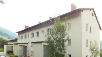 Mehrfamilienhaus mit heller Fassade und Satteldach in ländlicher Umgebung mit Bergblick.