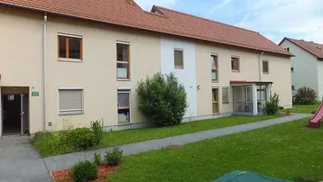Mehrfamilienhaus mit beiger Fassade, roten Ziegeldächern und gepflegter Rasenfläche im Vordergrund.