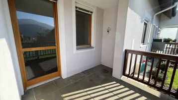 Sonniger Balkon mit Fliesenboden, Holzgeländer und Blick auf die Berge.