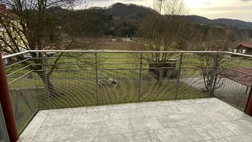 Balkon mit Fliesenboden und weitem Blick über die umliegende grüne Landschaft und Hügel.