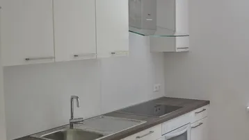 Helle, moderne Küche mit weißen Schränken, Induktionskochfeld und Parkettboden.