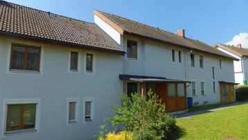 Ansicht der modernen Gebäudefassade mit Satteldach und gepflegter Grünfläche im Vordergrund.