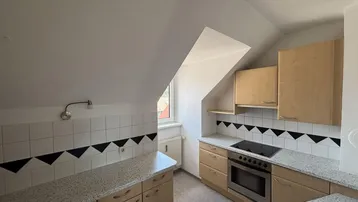 Dachgeschossküche mit heller Holzoptik, Granitarbeitsplatten und integriertem Kochfeld.