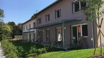 Moderne Reihenhäuser mit gepflegten Vorgärten und überdachten Terrassen unter blauem Himmel.