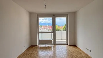 Heller Wohnraum mit Parkettboden, Balkonzugang und Bergblick in der Ferne.