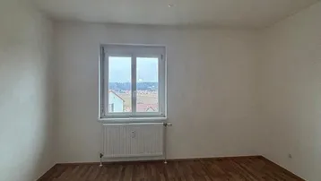 Heller, leerer Raum mit Laminatboden und einem Fenster, das eine weite Aussicht bietet.