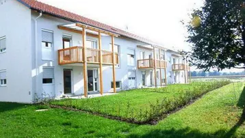 Modernes Mehrfamilienhaus mit weißer Fassade, Holzbalkonen und gepflegtem Rasenbereich.