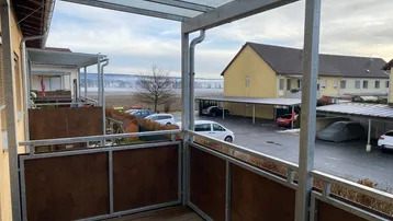 Balkon mit Holzboden, Metallgeländer und Blick auf die Umgebung und Parkplätze.