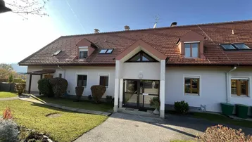 Gepflegtes Einfamilienhaus mit Satteldach, weißer Fassade und Vorgarten unter blauem Himmel.
