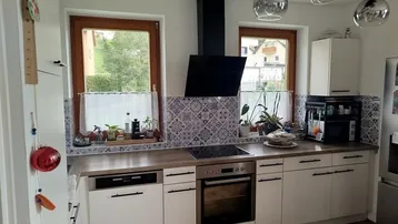 Moderne Küche mit weißen Schränken, integrierten Geräten und dekorativem Fliesenspiegel.