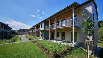 Moderne Reihenhäuser mit Holzfassade, Balkonen und kleinen Gärten in ländlicher Umgebung.