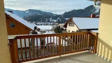 Balkon mit Holzbalken und Fliesenboden bietet einen weiten Blick auf die verschneite Berglandschaft.