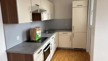 Funktionale Einbauküche mit hellen Fronten, dunkler Arbeitsplatte und Holzparkettboden.