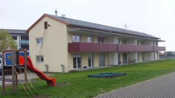 Mehrfamilienhaus mit Balkonen, einem kleinen Spielplatz und Grünfläche im Außenbereich.