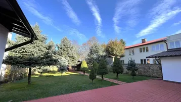 Gepflegter Gartenbereich mit rotem Pflasterweg, Rasenfläche und verschiedenen Nadelbäumen unter blauem Himmel.
