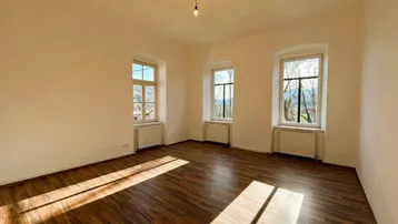 Lichtdurchfluteter Wohnraum mit Holzboden und Fenstern, die viel Tageslicht hereinlassen.