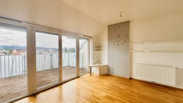 Geräumiges Wohnzimmer mit Holzboden, großer Fensterfront und Zugang zur Dachterrasse mit Stadtblick.