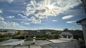 Weitblick über Dächer und grüne Landschaft unter einem sonnigen Himmel.
