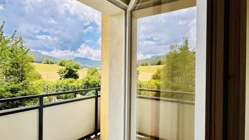 Balkon mit Fliesenboden und weitem Blick über grüne Hügel und Berge.