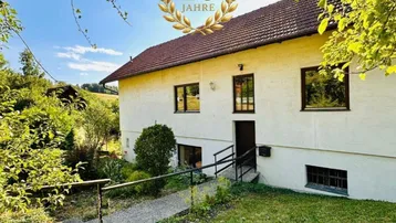 Ländliches Haus mit weißer Fassade und Garten in sonniger Umgebung.