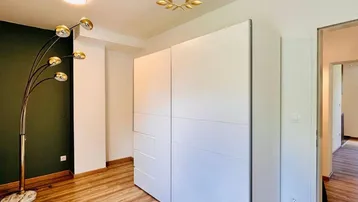 Helles Zimmer mit großem weißen Kleiderschrank, Holzboden und dunkler Akzentwand.