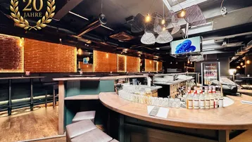 Moderne Bar mit Holztheke, freigelegten Ziegelwänden und stimmungsvoller Beleuchtung durch Oberlichter.