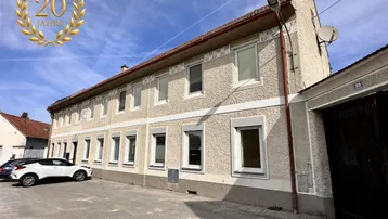 Gebäudeansicht mit Putzfassade und mehreren Fenstern, davor ein geparktes Auto auf dem Hof.