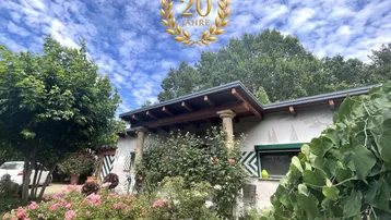 Eingangsbereich des Hauses umgeben von üppigem Grün und blühenden Rosensträuchern unter blauem Himmel.