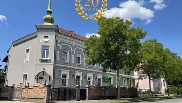 Historisches Gebäude mit markantem Turm, schmiedeeisernem Zaun und gepflegter Fassade.