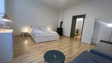 Helles Schlafzimmer mit Doppelbett, Sofa, Holzofen und hellem Holzfußboden.